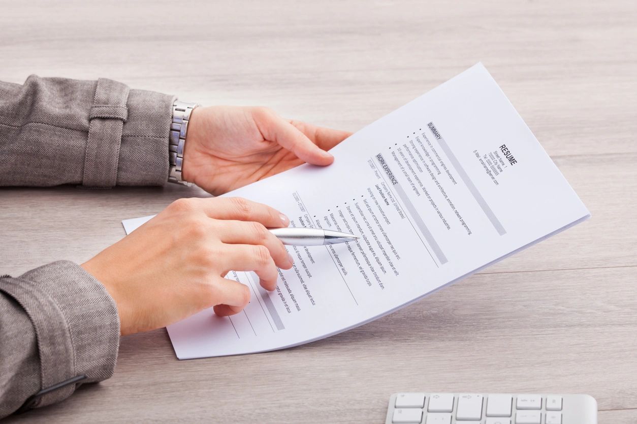 A person holding a paper and pen on top of a table.